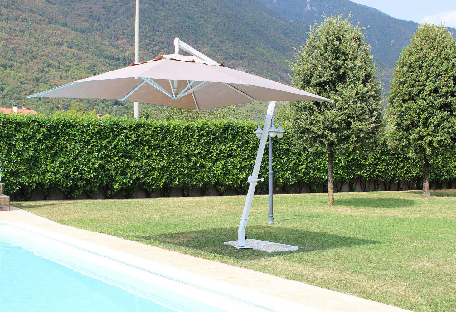 Ombrellone Pegaso aperto a bordo piscina durante il giorno, che proietta un'ampia zona d'ombra sul prato.
