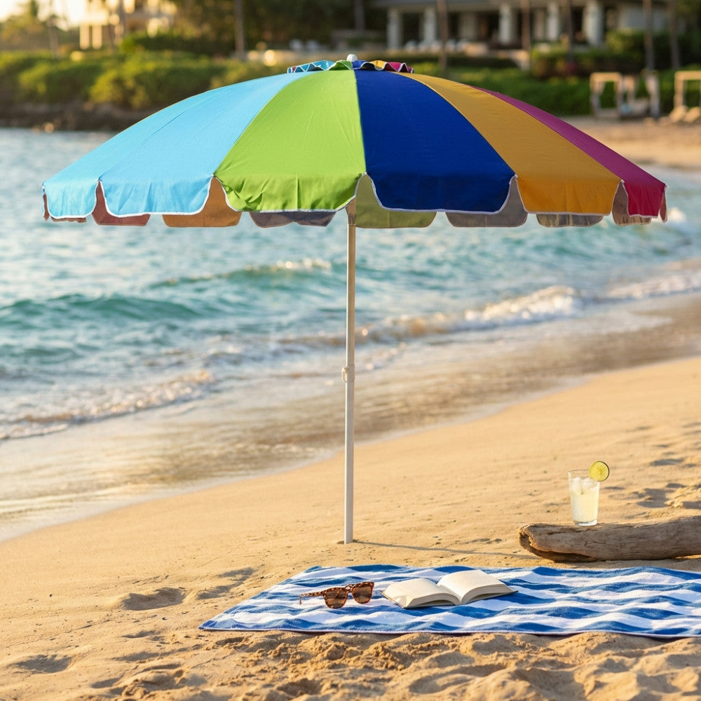 Ombrellone da spiaggia multicolor aperto sulla sabbia con telo mare a righe blu e bianche, occhiali da sole e libro.
