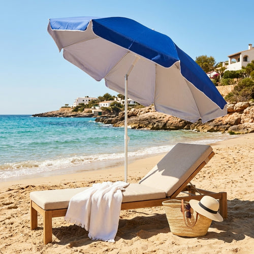Ombrellone da spiaggia blu aperto su una spiaggia sabbiosa, posizionato accanto a un lettino in legno di teak con asciugamano bianco e borsa in paglia.