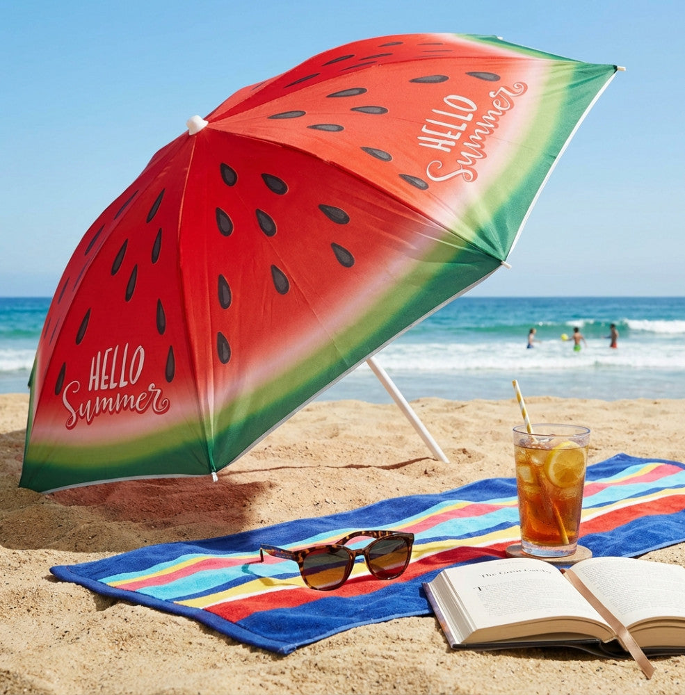 Ombrellone da spiaggia in poliestere con decoro ad anguria, aperto sulla sabbia accanto a un telo mare a righe, occhiali da sole e una bevanda ghiacciata.