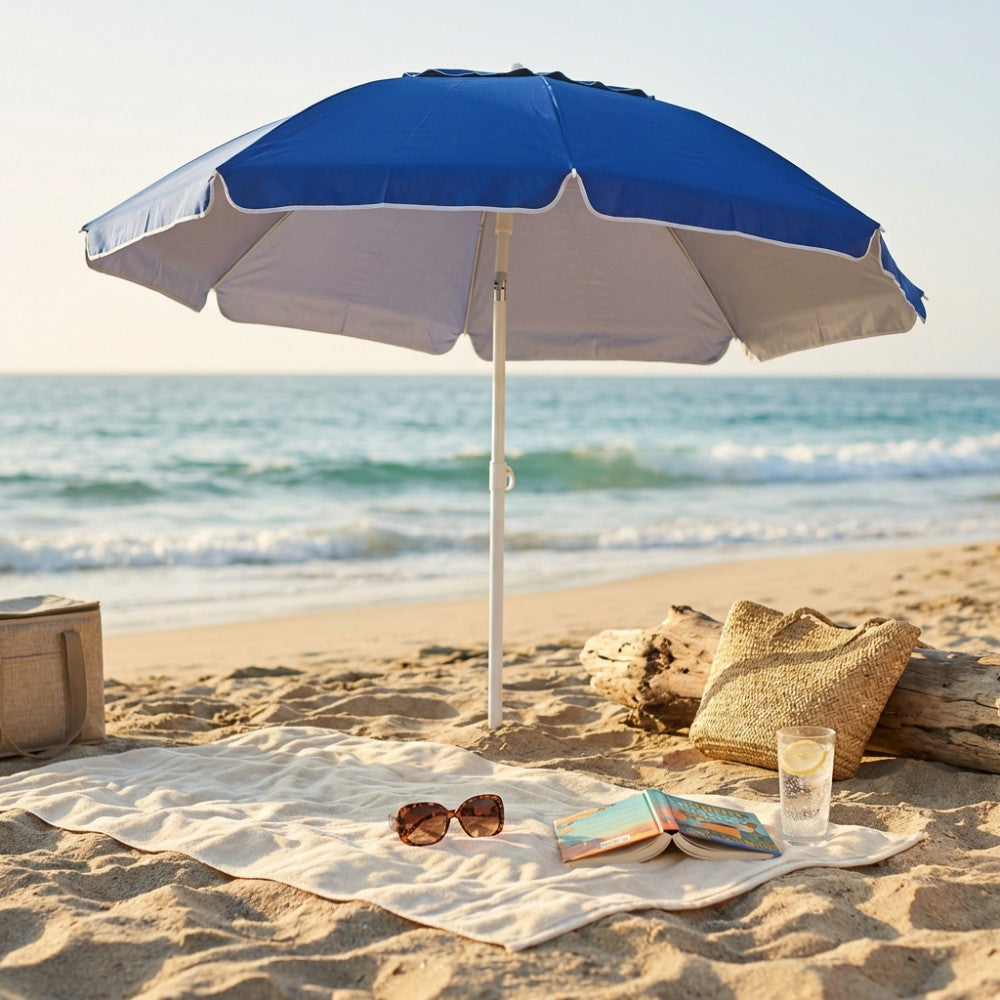 Ombrellone da spiaggia blu OM807041 aperto sulla sabbia, con telo mare, occhiali da sole e borsa in paglia.