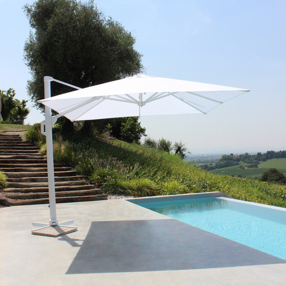 Il moderno ombrellone a braccio bianco posizionato elegantemente a bordo piscina, mostrando la sua solida base a croce e il profilo slanciato.