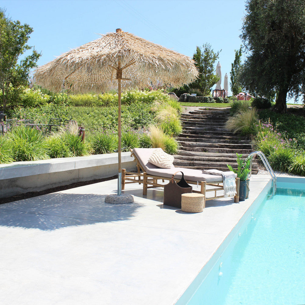 Ombrellone Tiki inserito in un lussuoso giardino a gradoni vicino a una piscina cristallina.