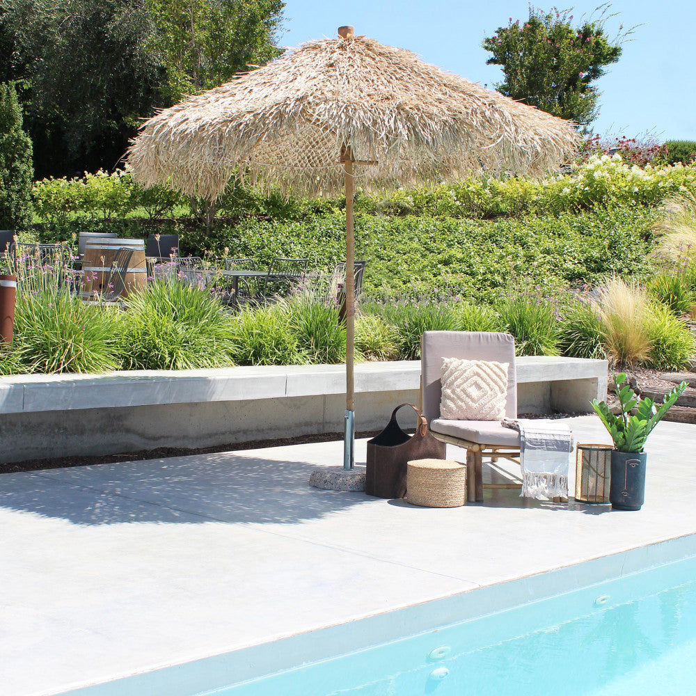 Ombrellone Tiki aperto in un patio soleggiato, abbinato a una poltroncina in bambù e accessori di design.