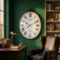 Orologio da parete ovale in acciaio e vetro stile vintage appeso in uno studio con pareti verdi, scrivania in legno e poltrona in pelle.