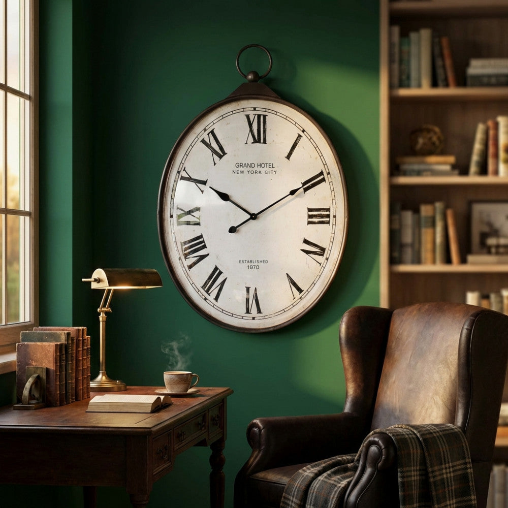 Orologio da parete ovale in acciaio e vetro stile vintage appeso in uno studio con pareti verdi, scrivania in legno e poltrona in pelle.