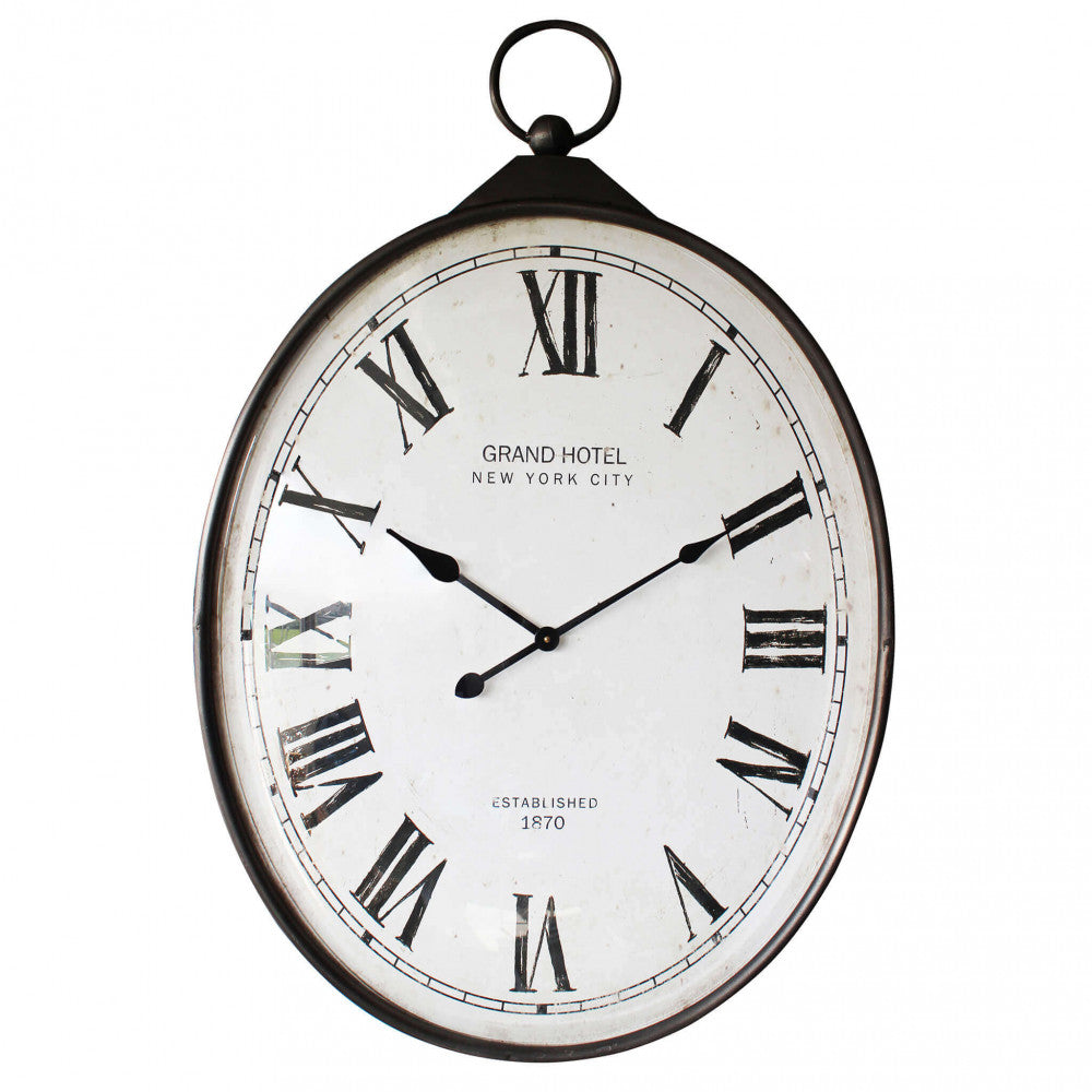 Dettaglio frontale dell'orologio da parete ovale su sfondo bianco, che evidenzia la struttura in acciaio scuro e il quadrante vintage.