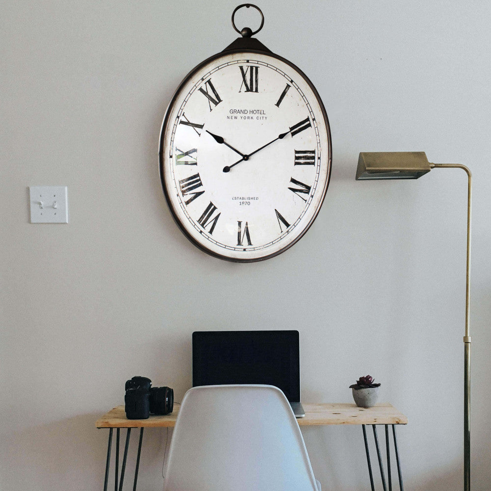 Orologio da parete vintage inserito in un ambiente minimalista sopra una scrivania moderna, affiancato da una lampada da terra in ottone.