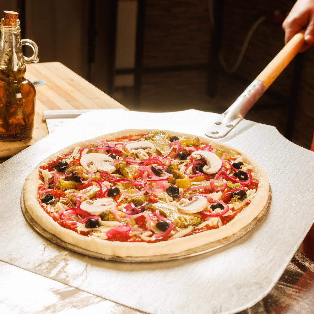 Primo piano della pala per pizza in metallo che solleva una pizza cruda e colorata alle verdure, dimostrando la sua pratica funzionalità e la costruzione di prima qualità.