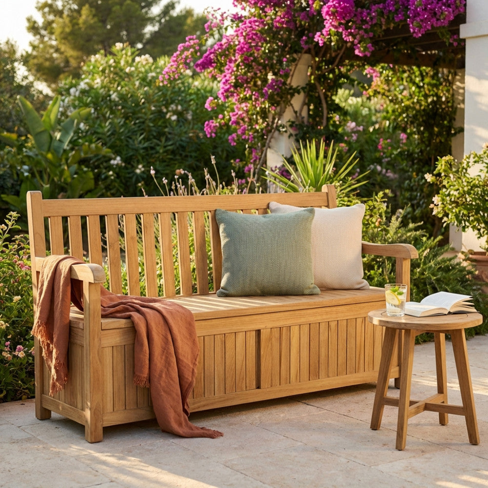 Panca in teak Surat allestita su un patio in pietra con cuscini decorativi e un tavolino laterale.