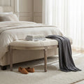 Panca Margi in tessuto beige posizionata ai piedi di un letto matrimoniale elegante.
