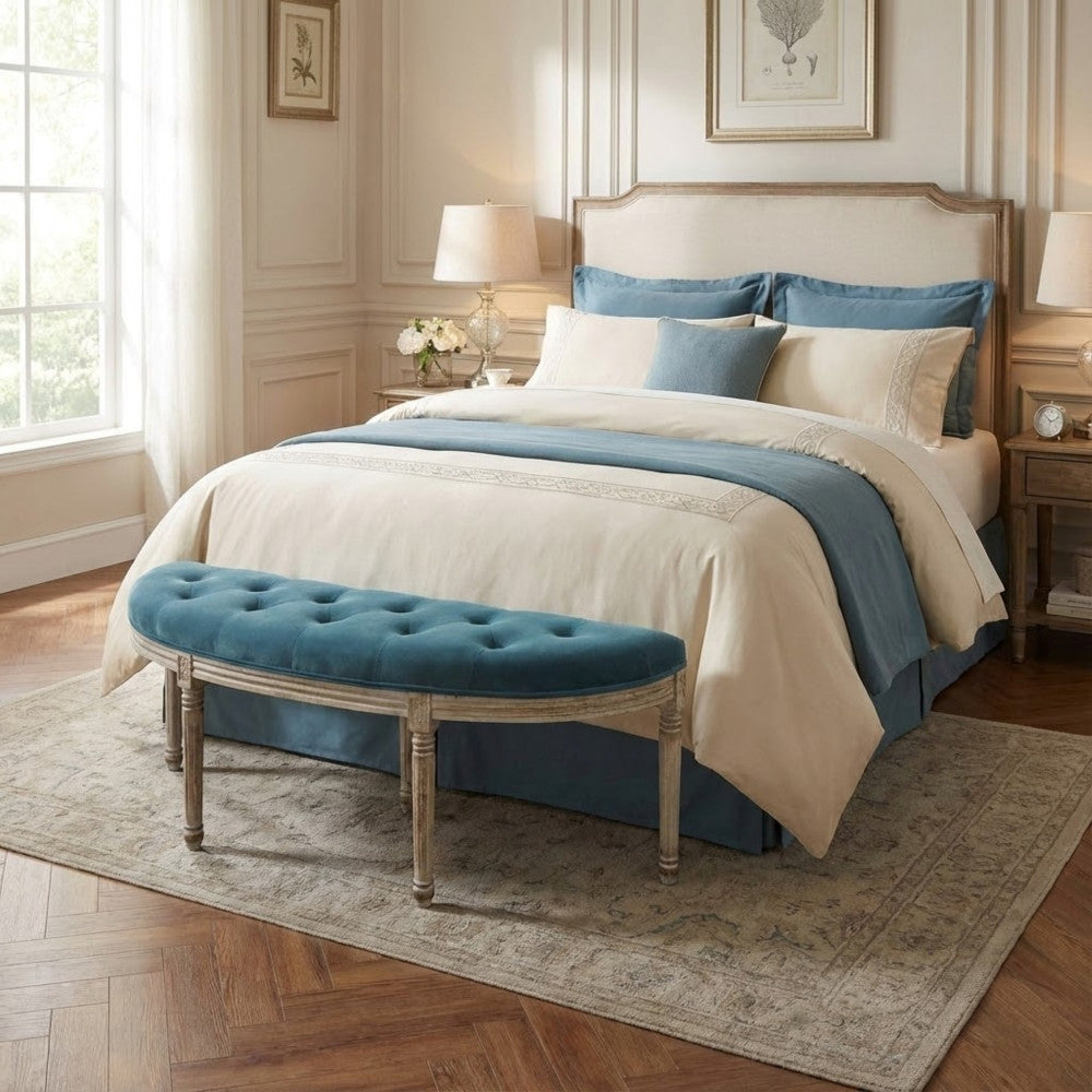 Panca in velluto blu posizionata ai piedi di un letto matrimoniale con biancheria coordinata.