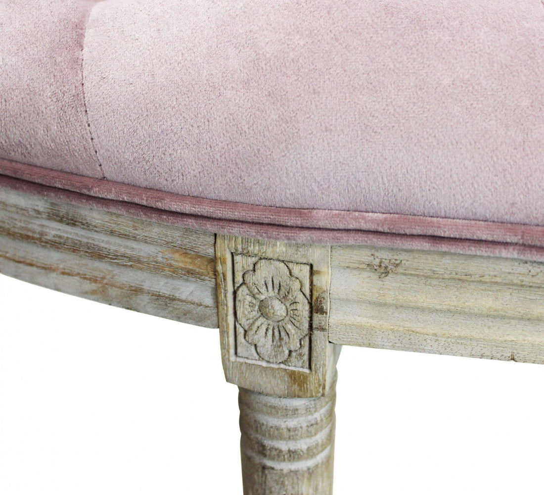 Primo piano del tessuto in velluto rosa e del dettaglio floreale intagliato nel legno della struttura.