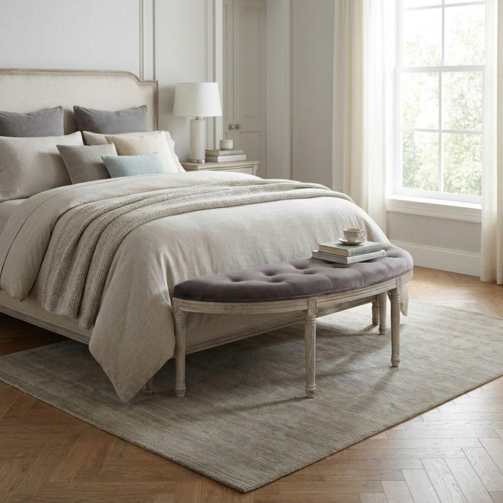 Panca Margi in velluto taupe ai piedi di un letto matrimoniale elegante con biancheria chiara.