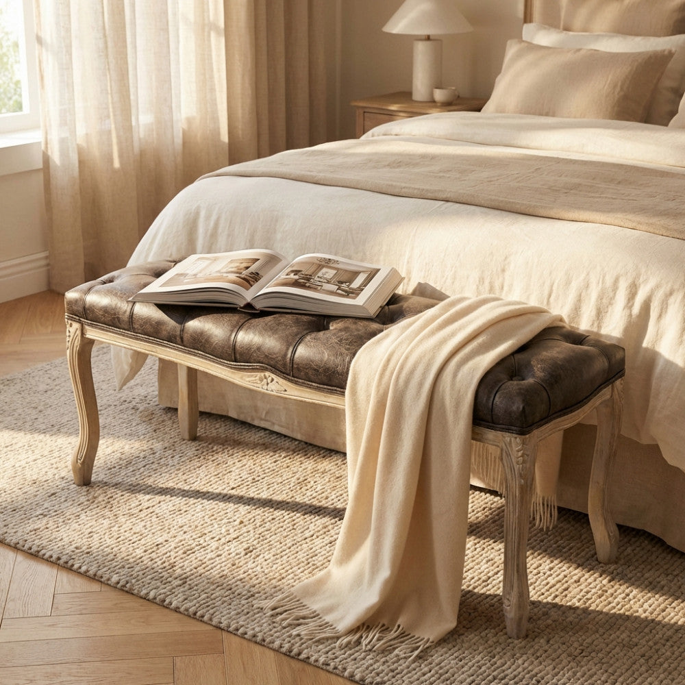 Panca Misty in ecopelle vintage taupe posizionata ai piedi di un letto matrimoniale elegante.