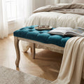 Panca Misty in velluto blu posizionata ai piedi di un letto con lenzuola in lino, decorata con un libro e occhiali.