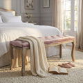 Panca in velluto rosa posizionata ai piedi di un letto matrimoniale con coperta in maglia.