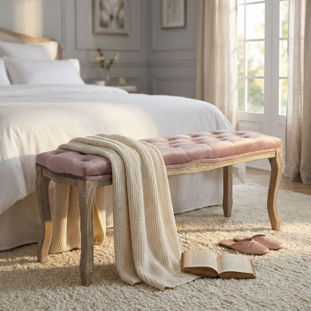 Panca in velluto rosa posizionata ai piedi di un letto matrimoniale con coperta in maglia.