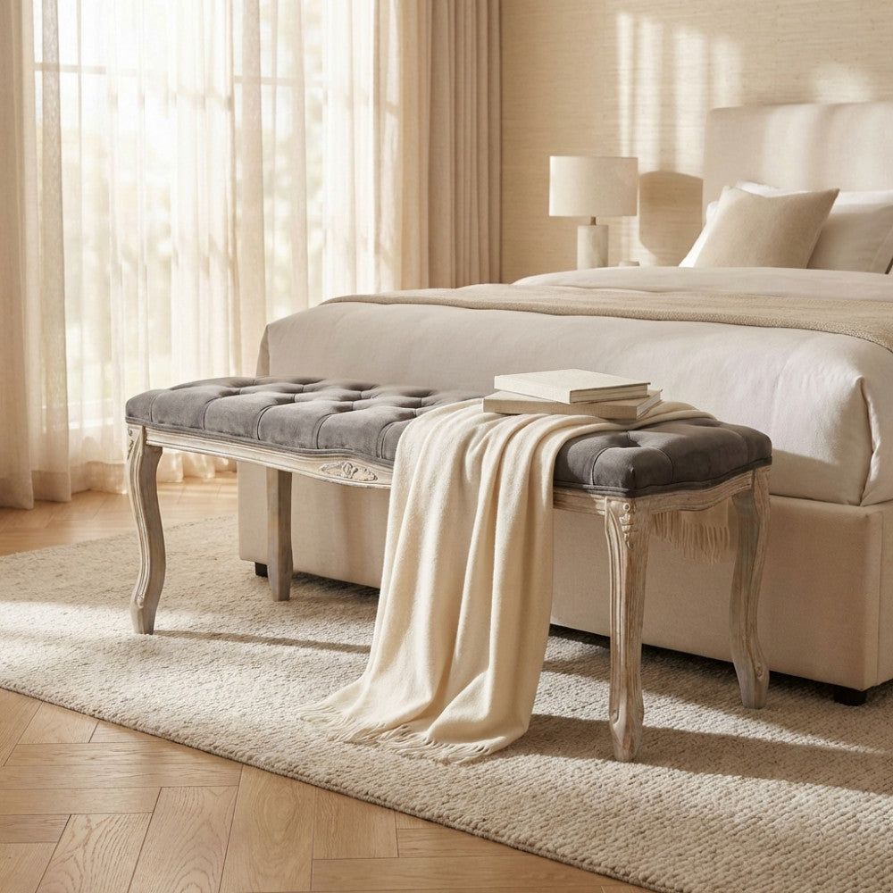 Panca da interno Misty in velluto taupe posizionata ai piedi di un letto matrimoniale con coperte chiare.