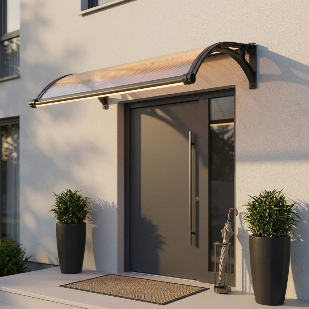 Pensilina in policarbonato grigio scuro installata sopra una porta d'ingresso moderna, illuminata dalla luce LED integrata al tramonto.