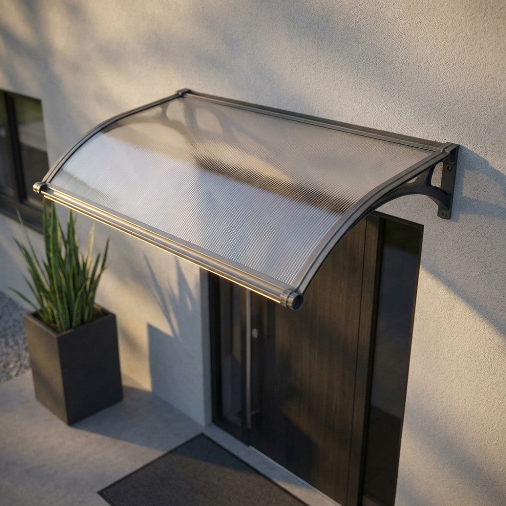 Pensilina in policarbonato opaco grigio scuro installata sopra un ingresso moderno con luce naturale.