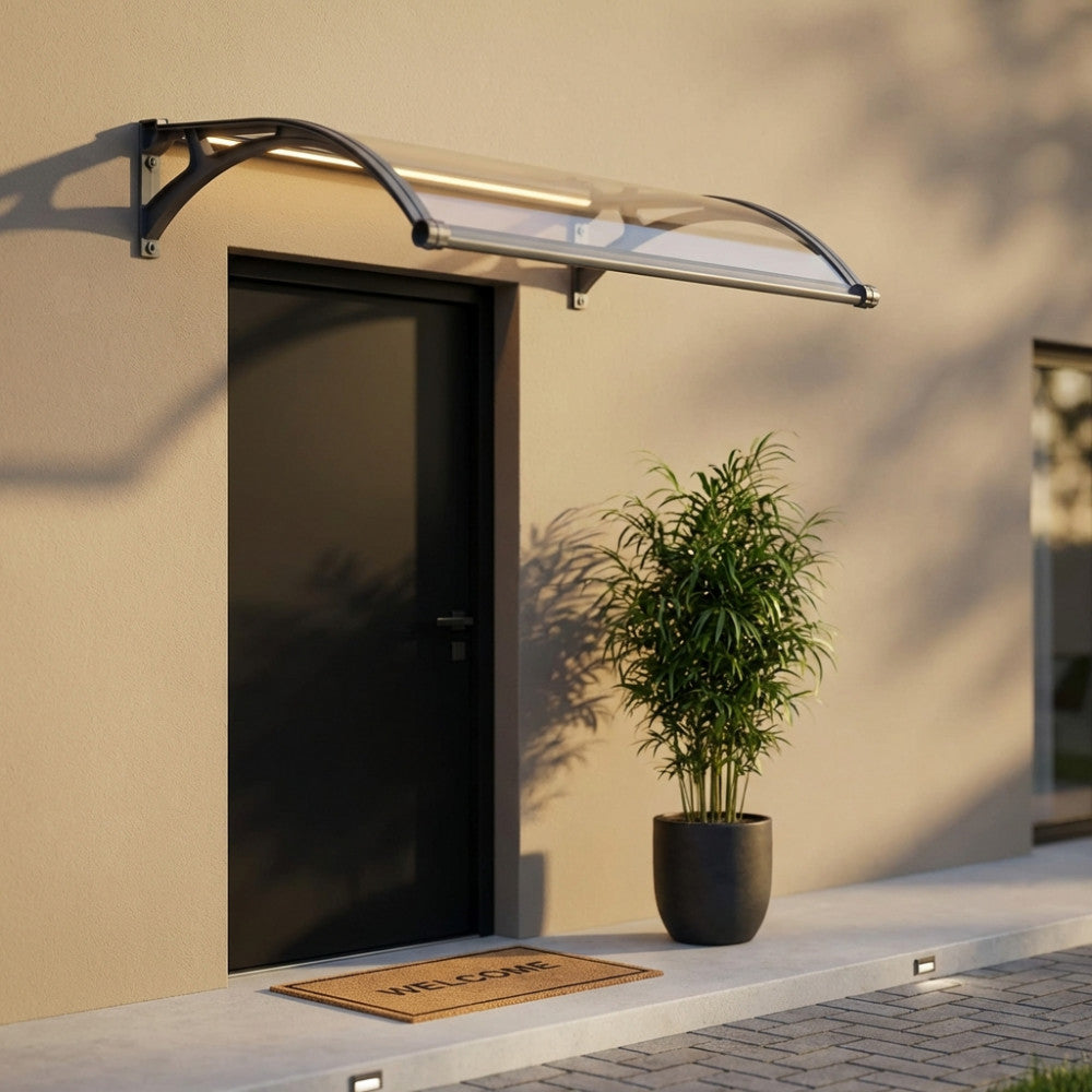 Pensilina Rainbow in policarbonato trasparente grigio con LED accesi, installata sopra una porta d'ingresso scura, illuminando un vaso con pianta verde.