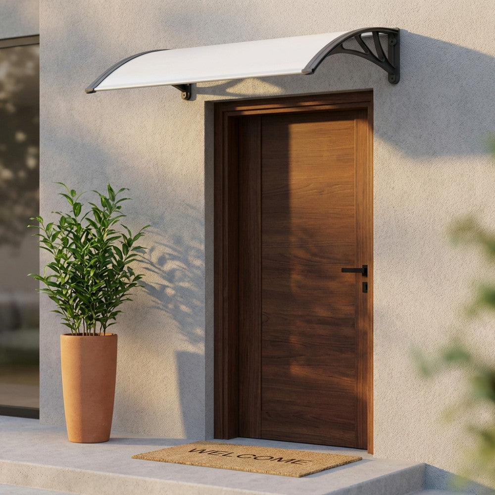 Pensilina Rain in policarbonato trasparente grigio installata sopra una porta d'ingresso in legno scuro, illuminata dalla luce solare.