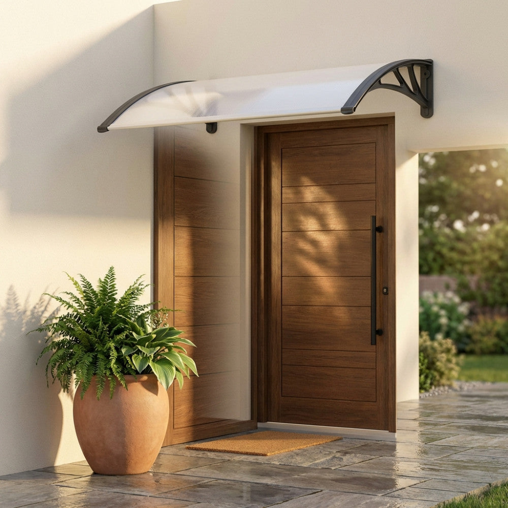 Pensilina in policarbonato trasparente grigio installata sopra una moderna porta in legno scuro, affiancata da un grande vaso in terracotta con felce.