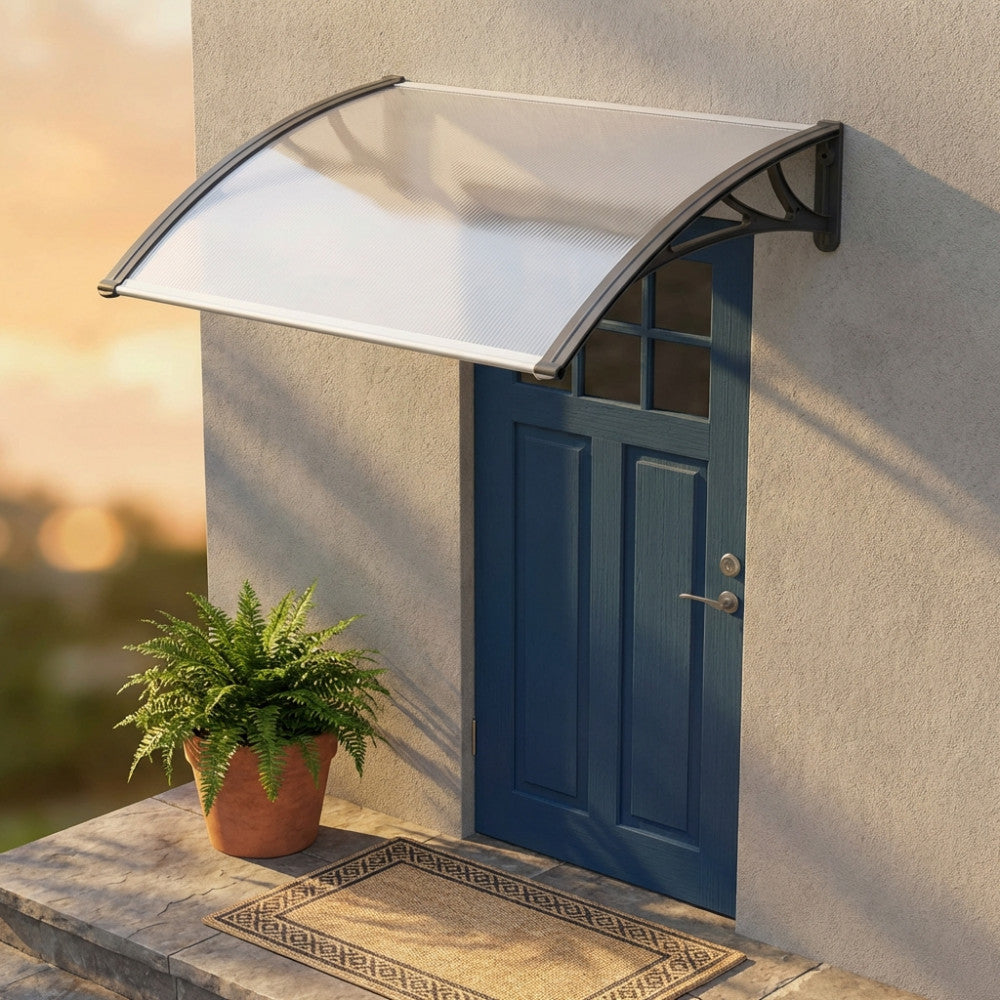 Pensilina curva in policarbonato montata sopra una porta d'ingresso blu, illuminata dalla calda luce del tramonto.