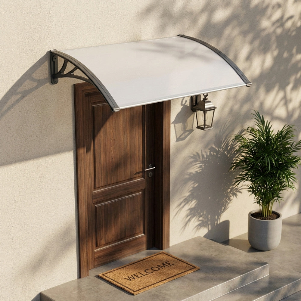 Pensilina RAIN in policarbonato installata sopra una porta in legno classica, con luce naturale che crea ombre morbide sulla facciata.