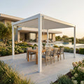 Pergola bioclimatica in alluminio bianco allestita con tavolo da pranzo in teak e sedie in un giardino lussuoso.