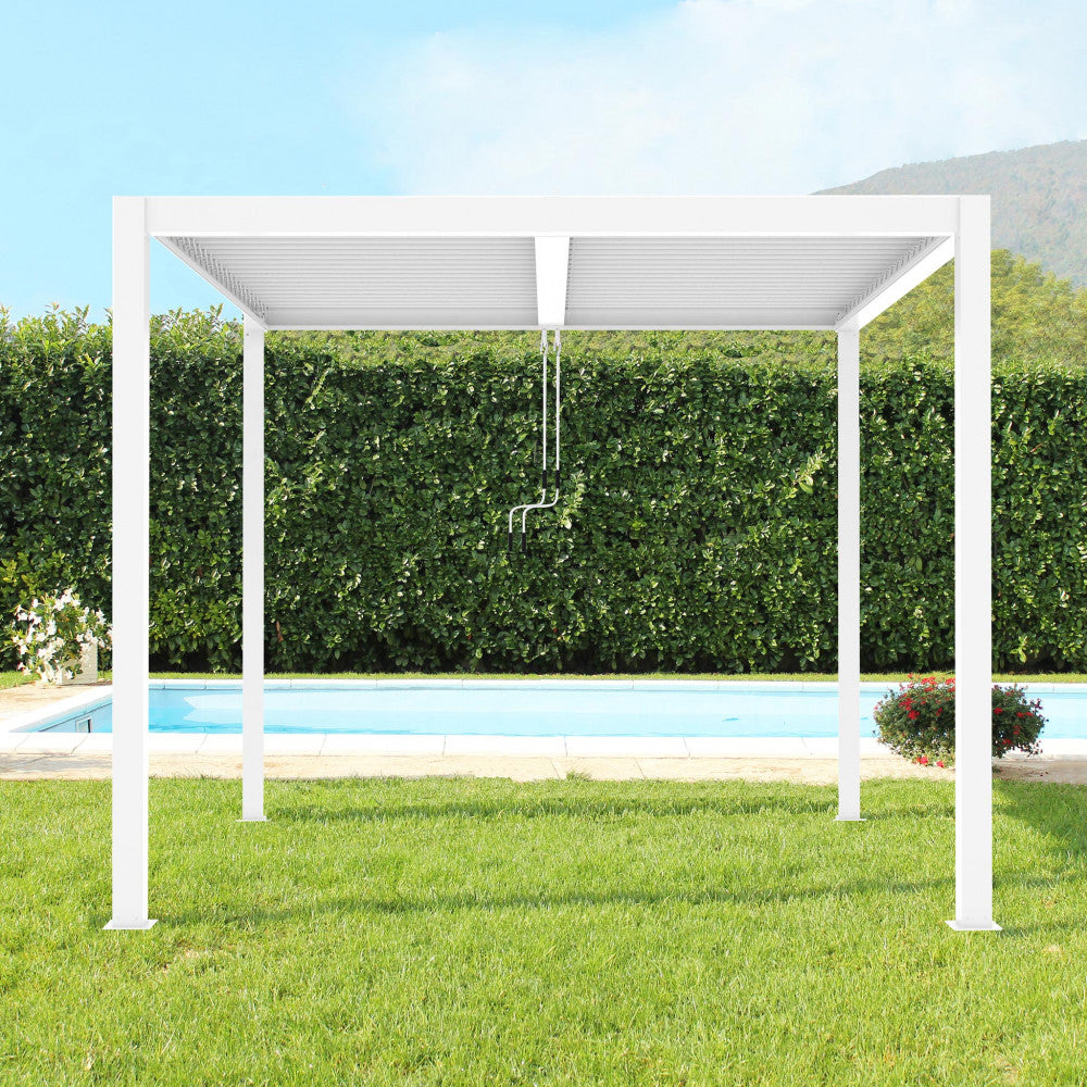Pergola bioclimatica in alluminio bianco installata su un prato verde vicino a una piscina con siepe sullo sfondo.