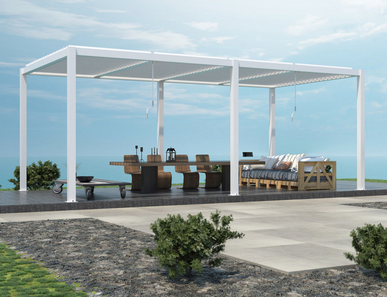 Pergola bioclimatica bianca installata su una terrazza panoramica con vista mare, arredata con tavolo scuro e divano in legno.