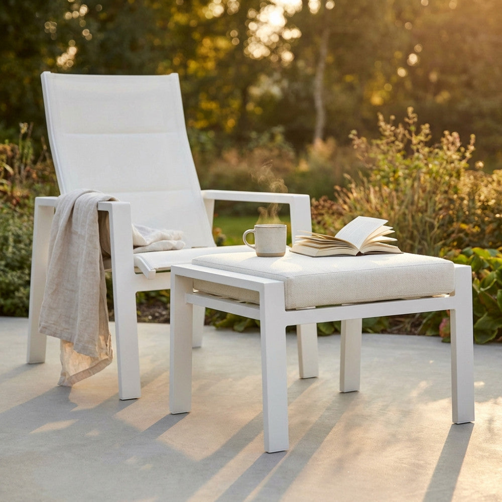 Poggiapiedi Giacarta in alluminio bianco affiancato a una poltrona lounge in un giardino illuminato dal sole.