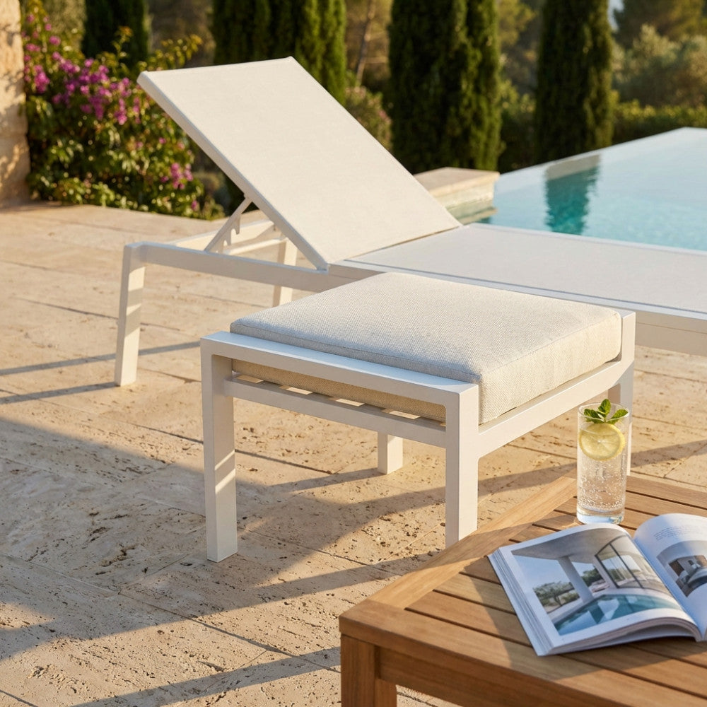Dettaglio del poggiapiedi moderno bianco a bordo piscina con un bicchiere d'acqua e un libro.