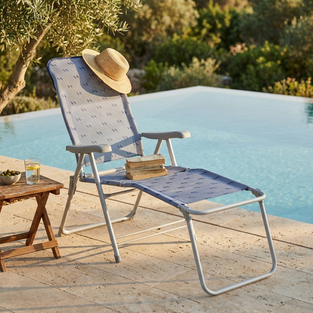 Sedia a sdraio Ischia con poggiapiedi, cappello di paglia e libri, in un'ambientazione outdoor soleggiata.