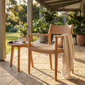 Poltrona Agra in teak e wicker ambientata in un patio esterno con tavolino e coperta in lino.