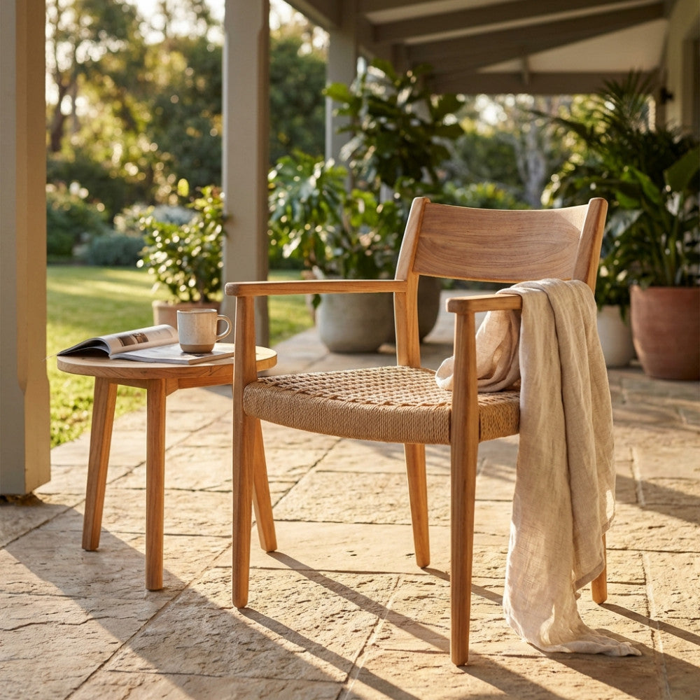 Poltrona Agra in teak e wicker ambientata in un patio esterno con tavolino e coperta in lino.
