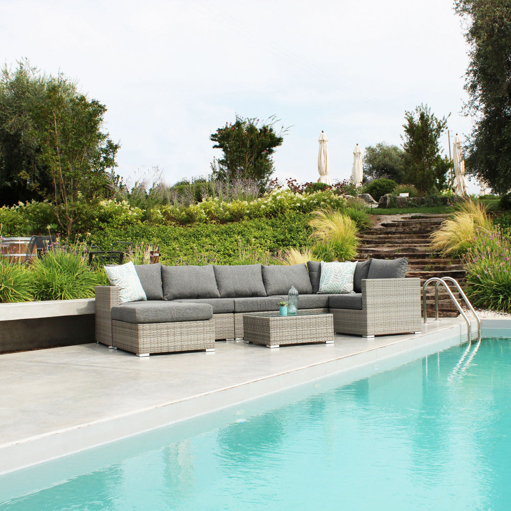 Set da esterno modulare Copacabana con poltrona angolare, tavolino e pouf, allestito elegantemente vicino a una piscina cristallina.