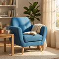 Poltrona Burton in tessuto blu ambientata in un luminoso soggiorno moderno, affiancata da un tavolino in legno con libro e tazza.
