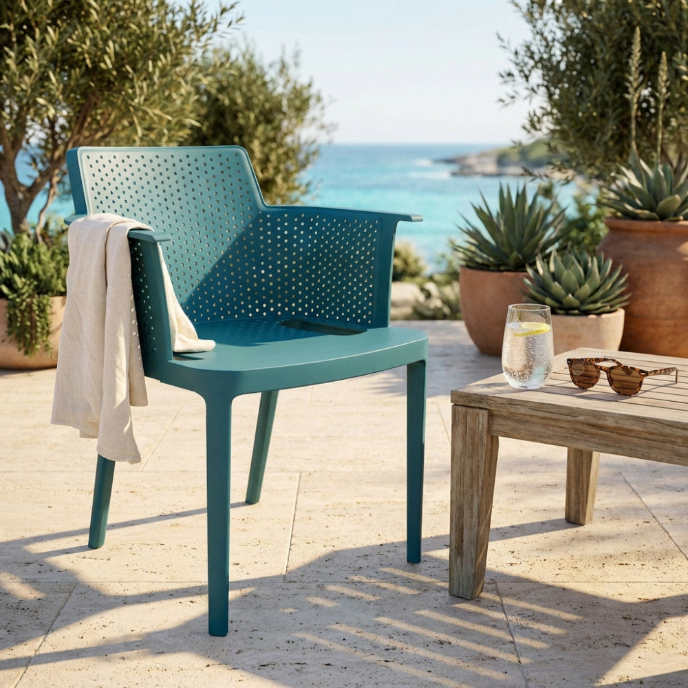Poltrona Cathy in polipropilene verde petrolio ambientata su una terrazza in pietra con vista mare.