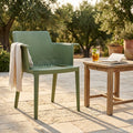 Poltrona Cathy in polipropilene verde ambientata in un giardino soleggiato con tavolino in teak.