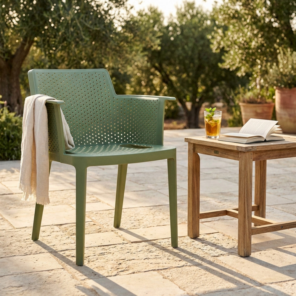 Poltrona Cathy in polipropilene verde ambientata in un giardino soleggiato con tavolino in teak.