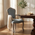 Poltrona Charlene in velluto grigio ambientata in una sala da pranzo elegante, accostata a un tavolo in legno scuro con un libro e una tazza da tè.