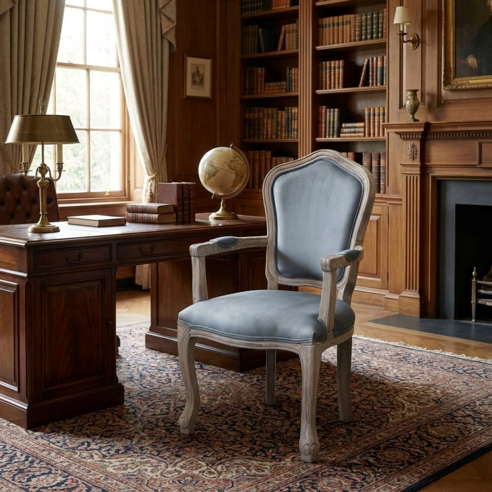 Poltrona in velluto grigio inserita in uno studio classico con boiserie in legno scuro, libreria, scrivania e un mappamondo.