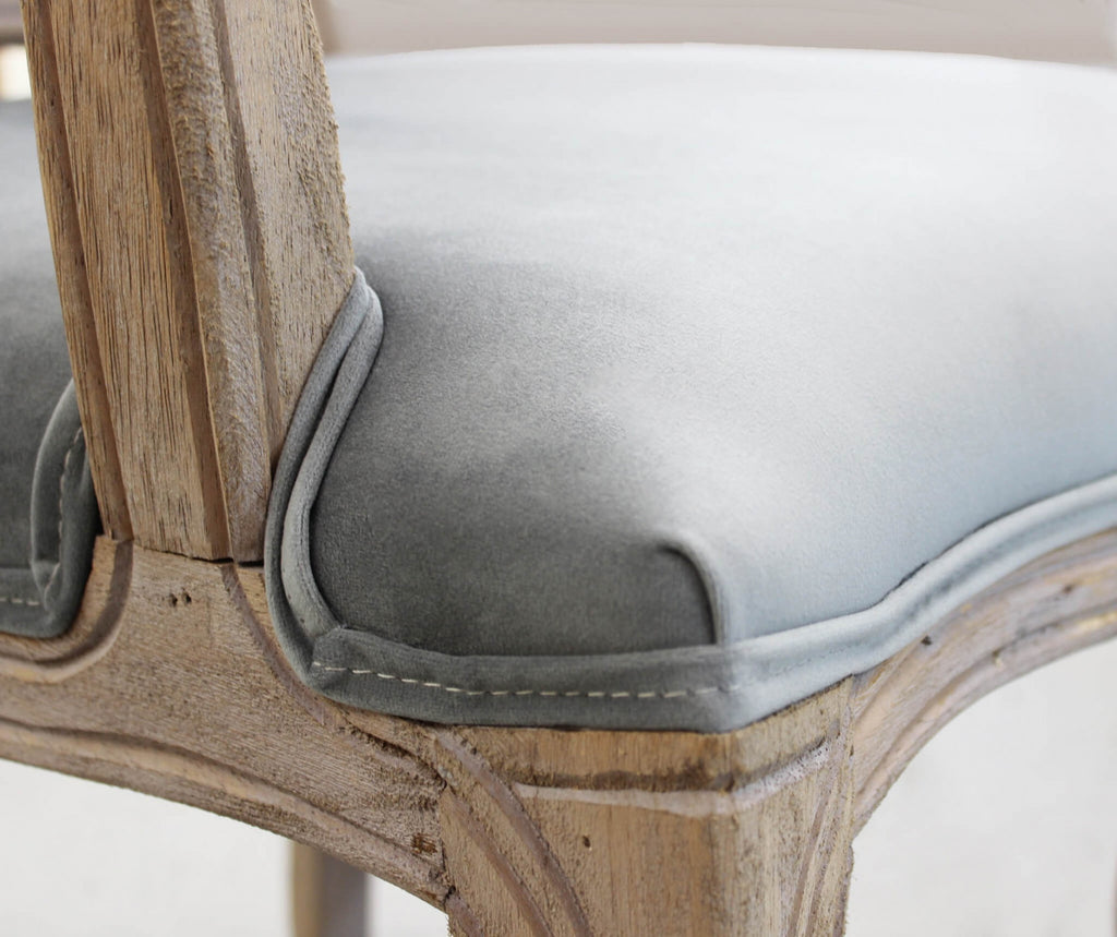 Dettaglio ravvicinato della seduta in velluto grigio, che mostra le cuciture, il cordino di finitura e l'intaglio del legno sulla gamba.