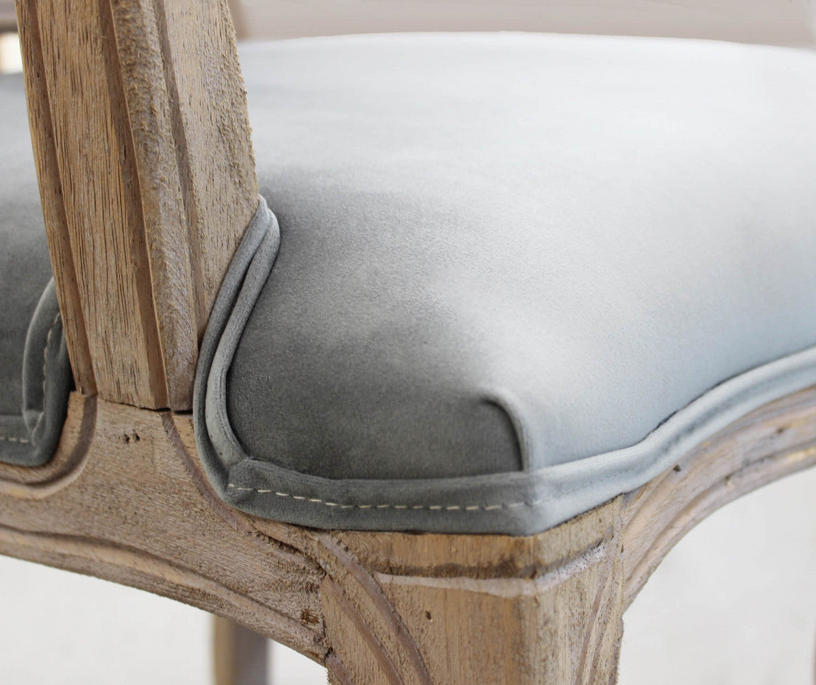 Dettaglio ravvicinato della seduta in velluto grigio, che mostra le cuciture, il cordino di finitura e l'intaglio del legno sulla gamba.