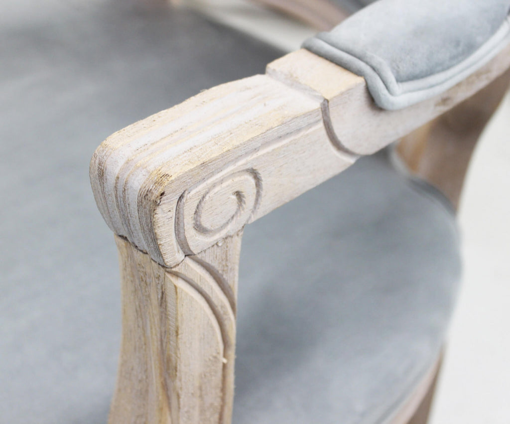 Primo piano del bracciolo della poltrona, con imbottitura in velluto e struttura in legno chiaro con finitura anticata e dettagli scolpiti.