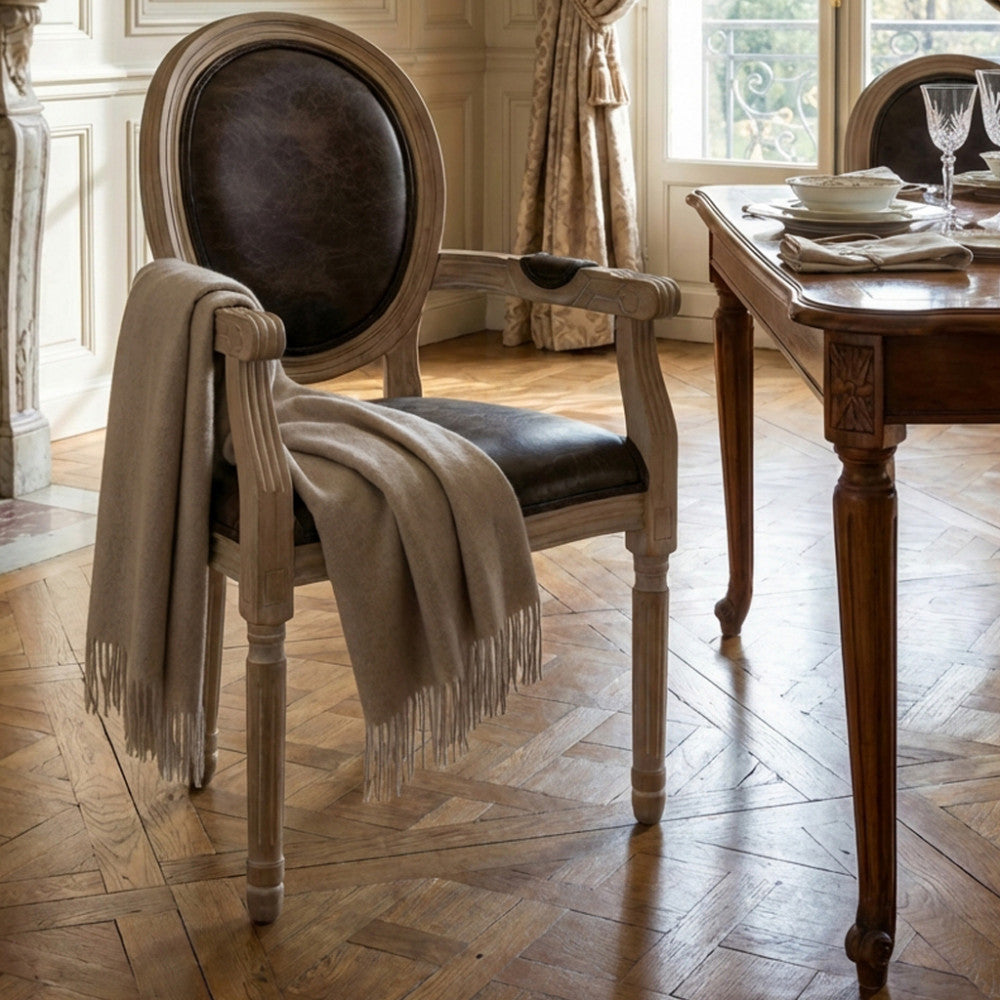 Poltrona classica con braccioli e un elegante plaid beige appoggiato, in un salone luminoso.