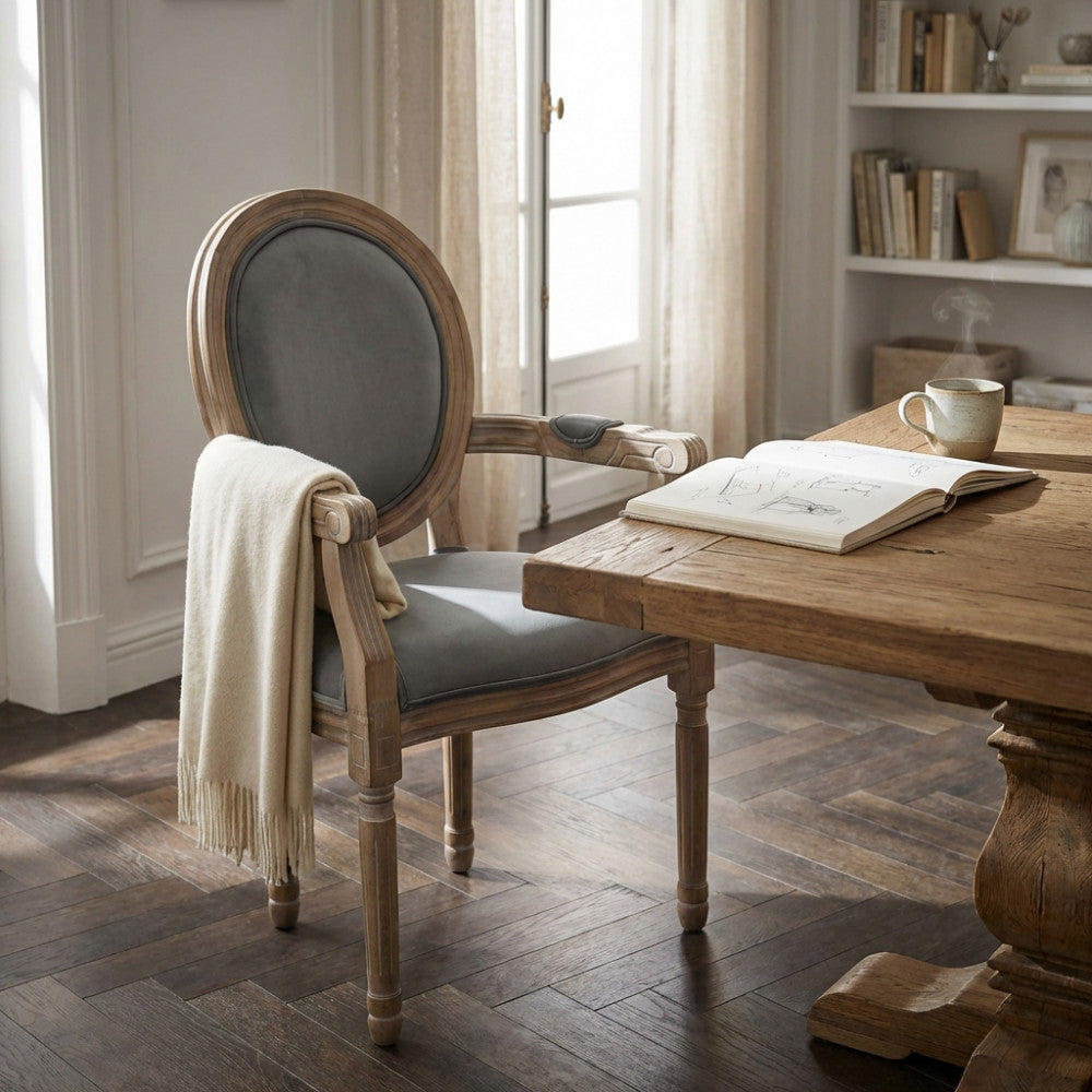 Poltrona Constance in velluto grigio ambientata accanto a un tavolo in legno massello con un libro aperto.